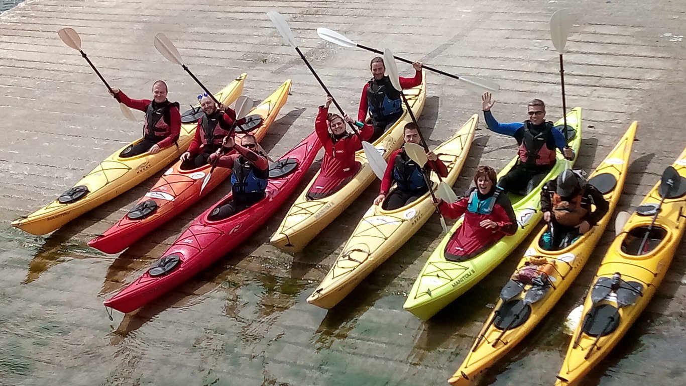 Kayaking group hold their paddles and wave in Dingle, Ireland