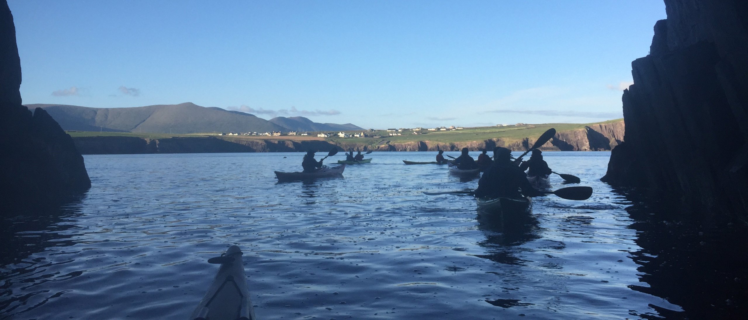 A group of kayakers paddling out of a sea cave in Dingle Bay, Ireland