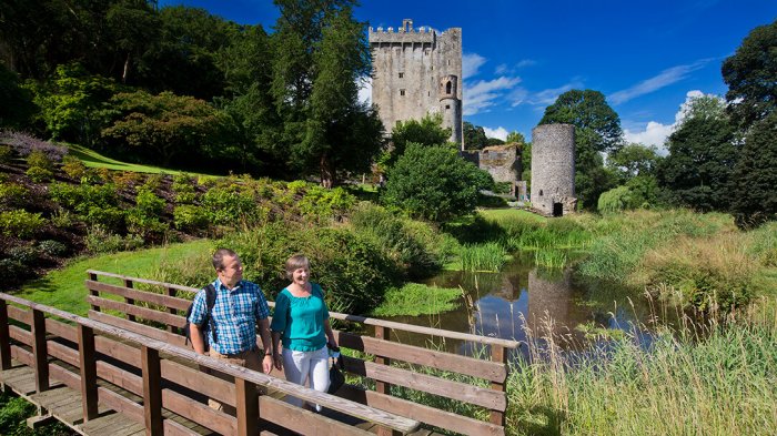 A couple walking across the bridge in Blarney Gardens with Blarney Castle in the background