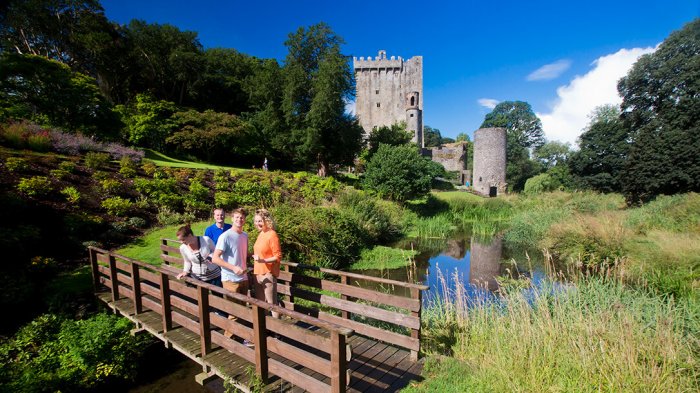 Two women and two men crossing the bridge in Blarney Gardens with Blarney Castle in the background