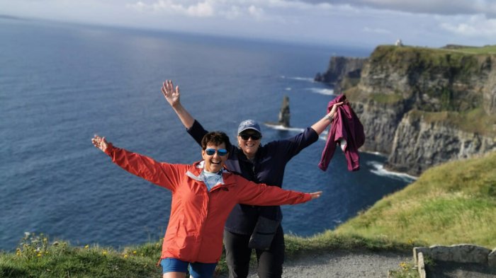 Two women with their hands in the air laughing with the Cliffs of Moher in the background