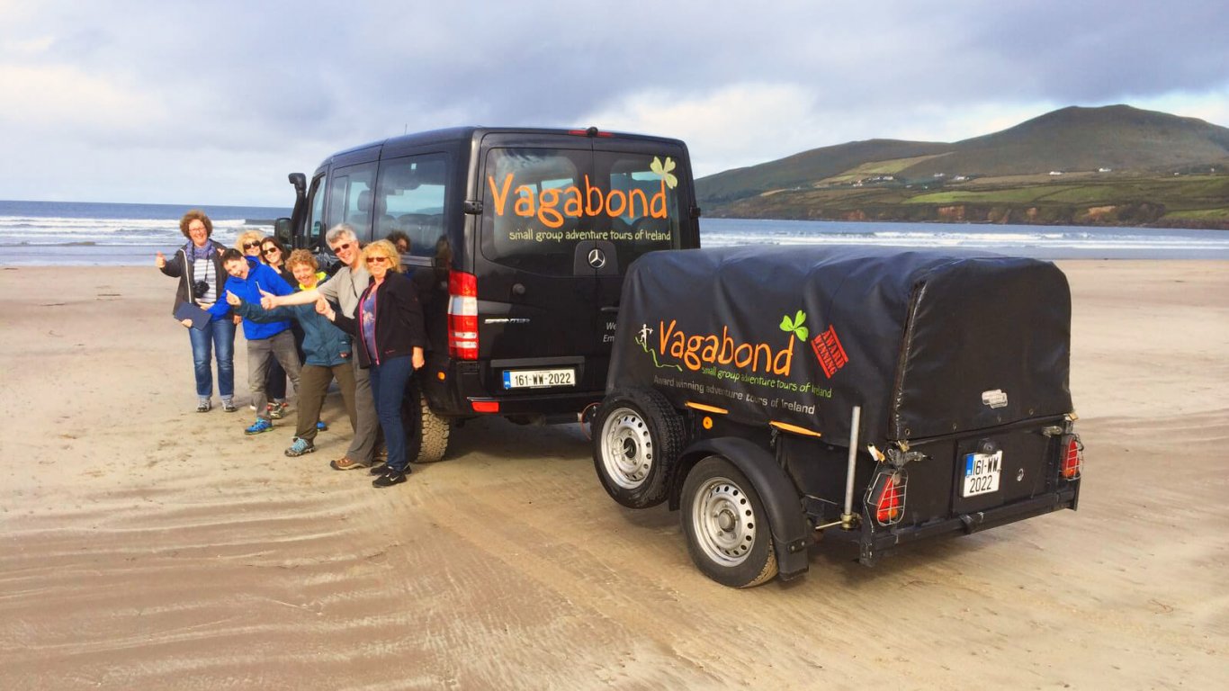 Group on the sand of Inch beach in ireland with their tour vehicle