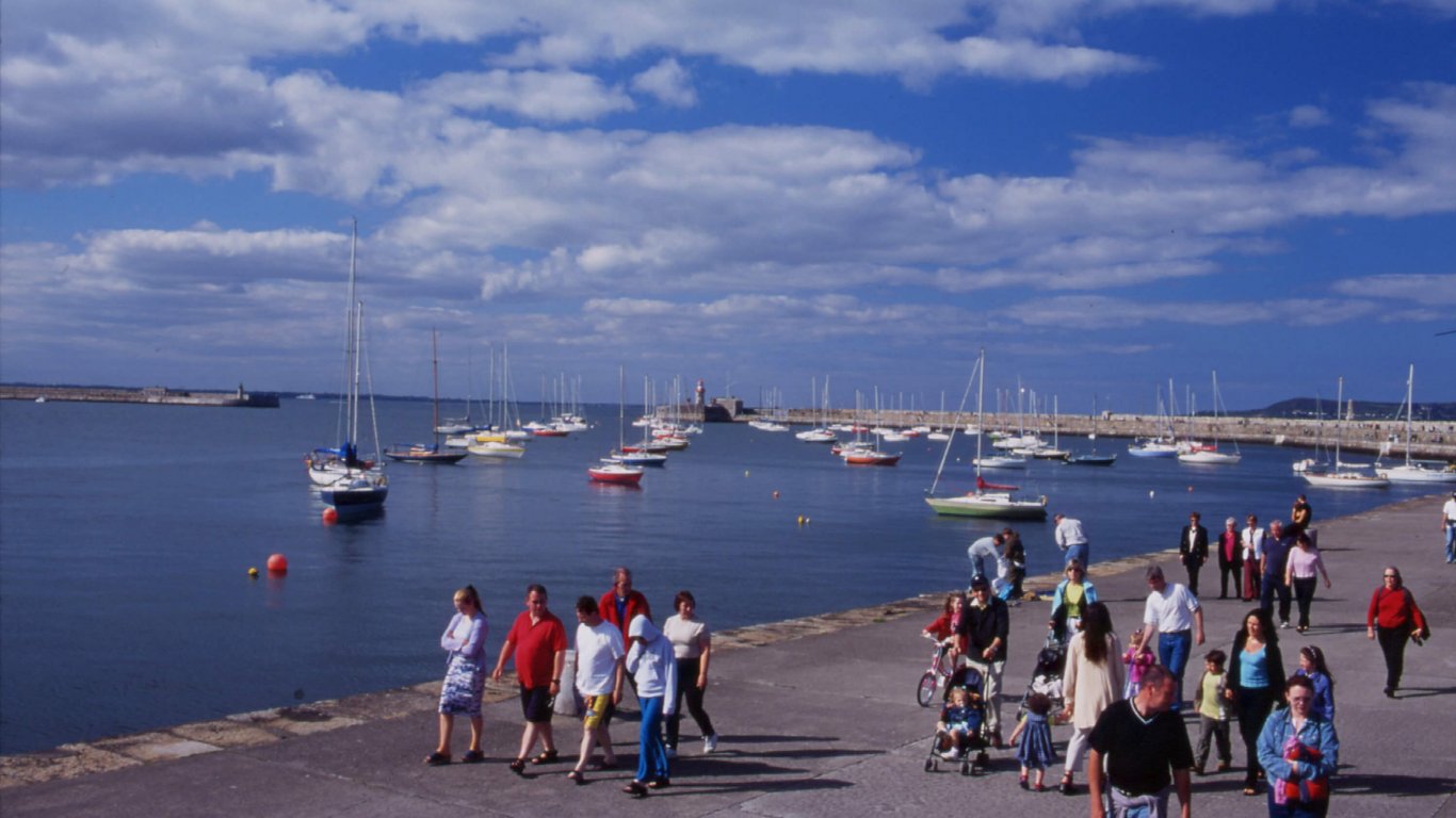 A view of Dun Laoghaire Harbour with boats sailing in the sunshine and people walking on the pier