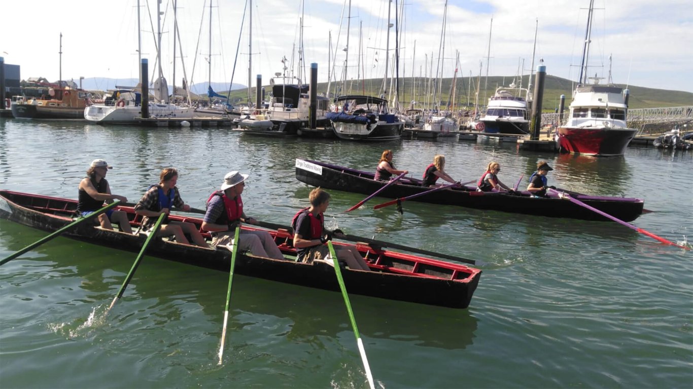 Two teams rowing Naomhóg boats in Dingle harbour