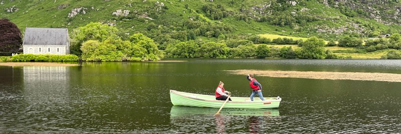 A couple in a green rowboat on a lake with a church in the background in Ireland