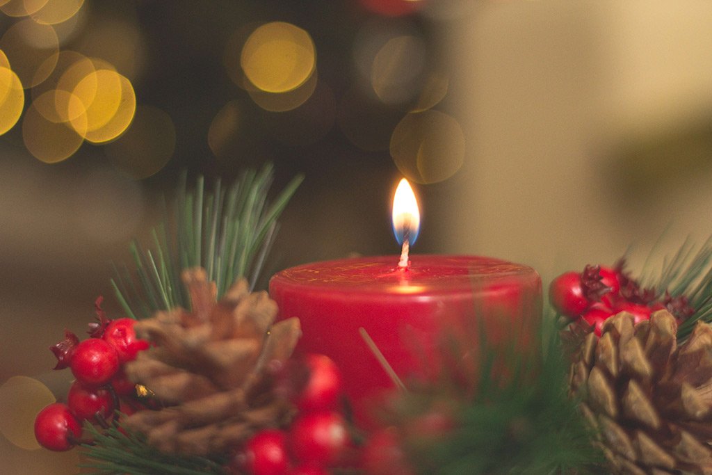 A red candle lighting surrounded by a wreath 