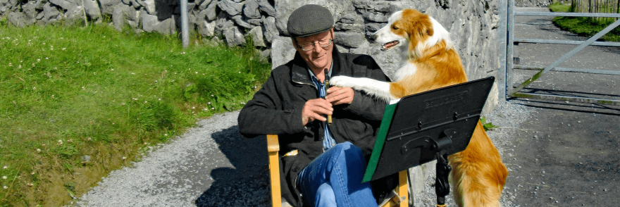 An Irish man sitting in the front garden playing the tin whistle accompanied by his dog