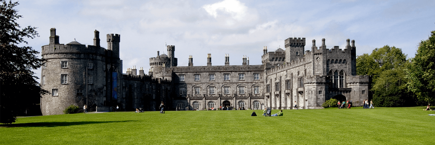 The exterior front of Kilkenny Castle with a view of the lawn and trees surrounding the castle