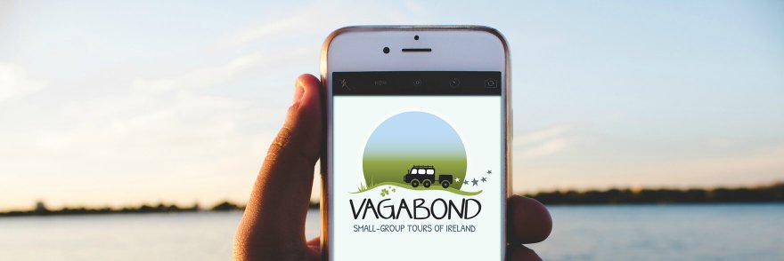 A hand holding a phone showing Vagabond logo on the screen with the sea in the background