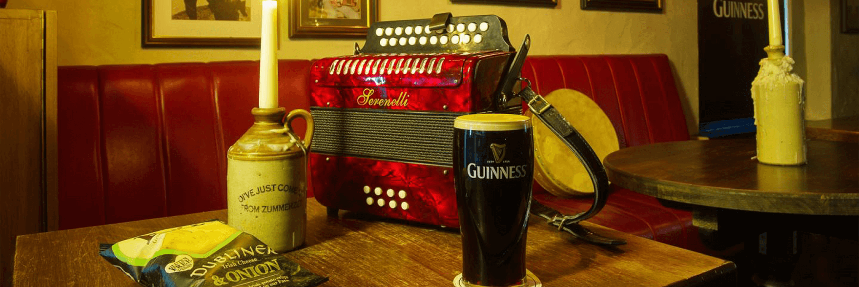 A pint of Guinness sitting on a table in an old Irish pub surrounded by a candle, crisps and an old instrument 