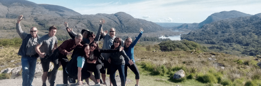 A group of Vagabond guests cheering with their arms in the air at Ladies View, Killarney National Park