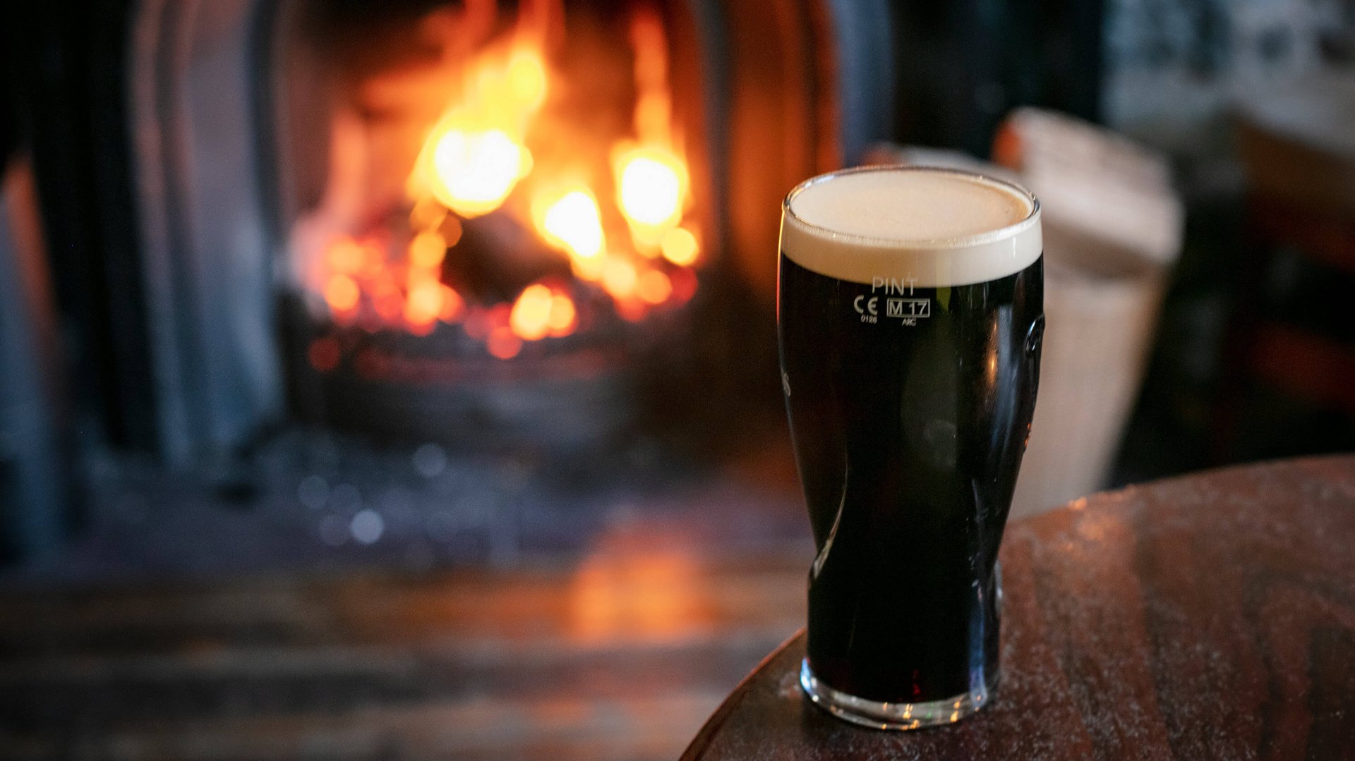 A pint of Guinness sitting on a table in front of a lighting fire