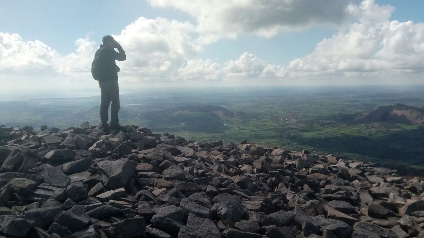 A man standing on the summit of Slieve Gullion looking down over the landscape