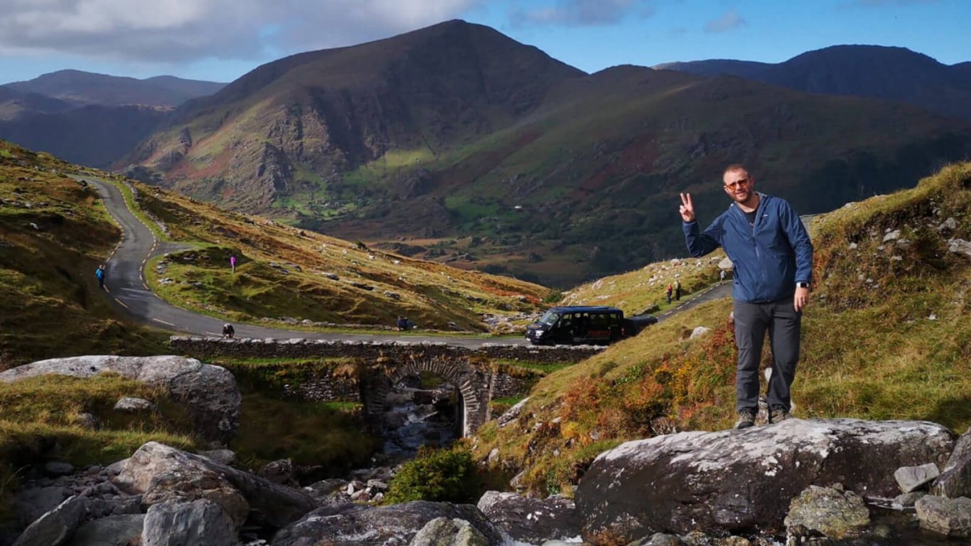 Vagabond Tours guest poses in front of tour vehicle and mountains in background