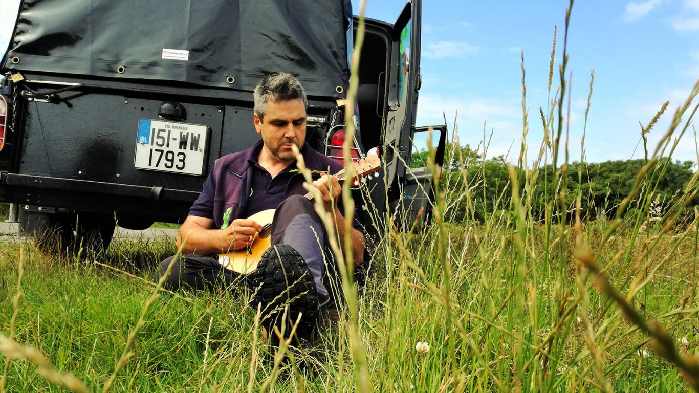 VagaGuide Tim relaxes beside tour vehicle while playing music in Ireland