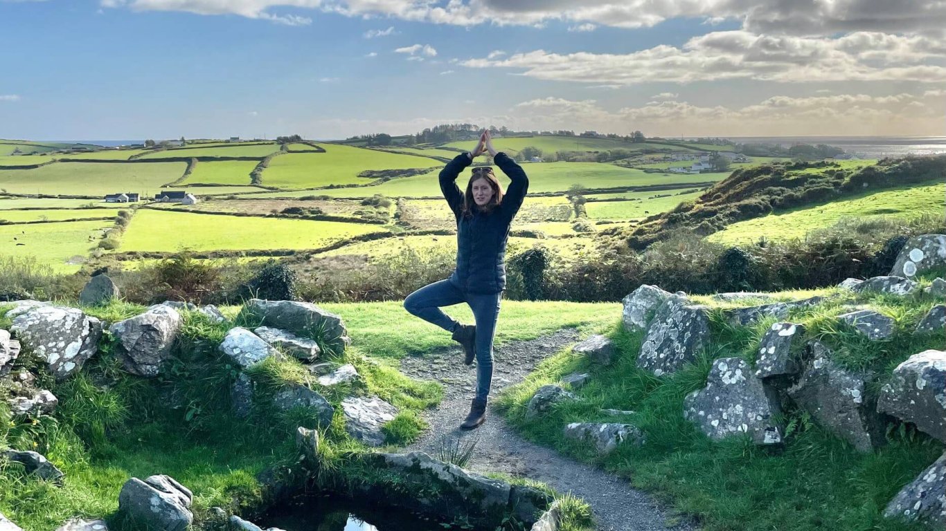 Edwina the Vagabond tour guide doing tree pose in scenic Irish landscape 