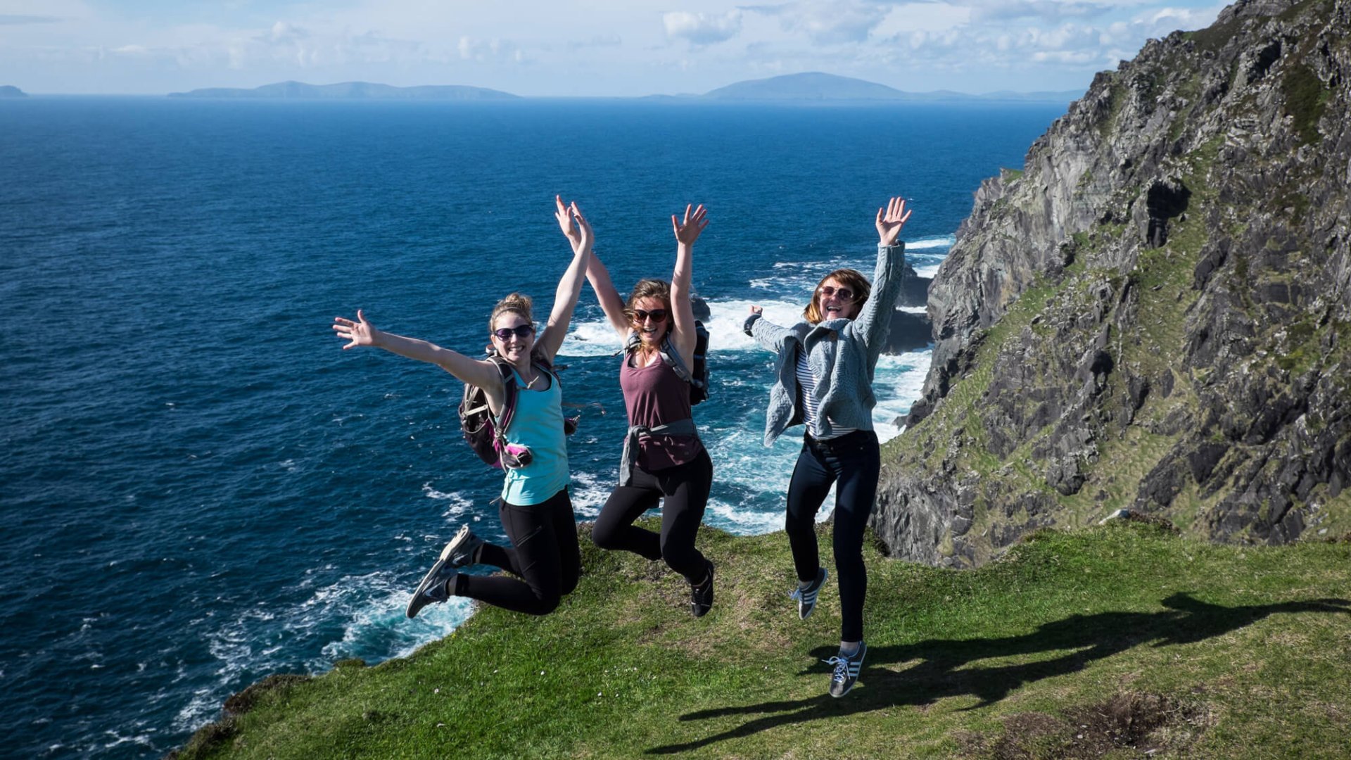 Three women jumping for joy with their arms in the air in the sunshine on Bray Head 