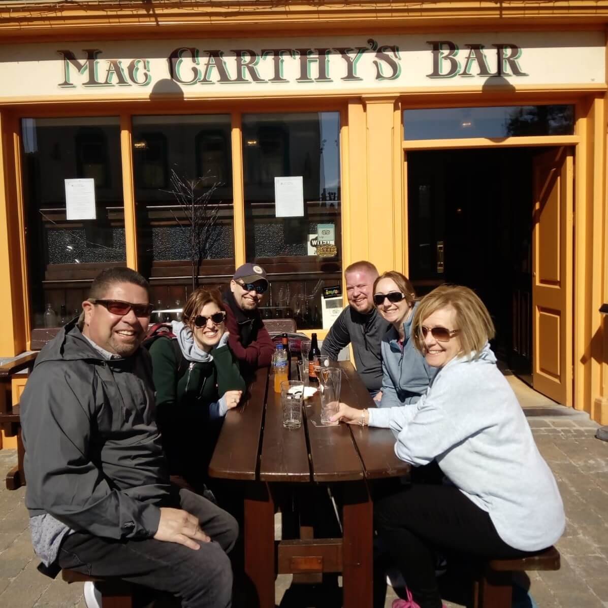 Happy tour group sitting outside McCarthy's pub during summer in Ireland