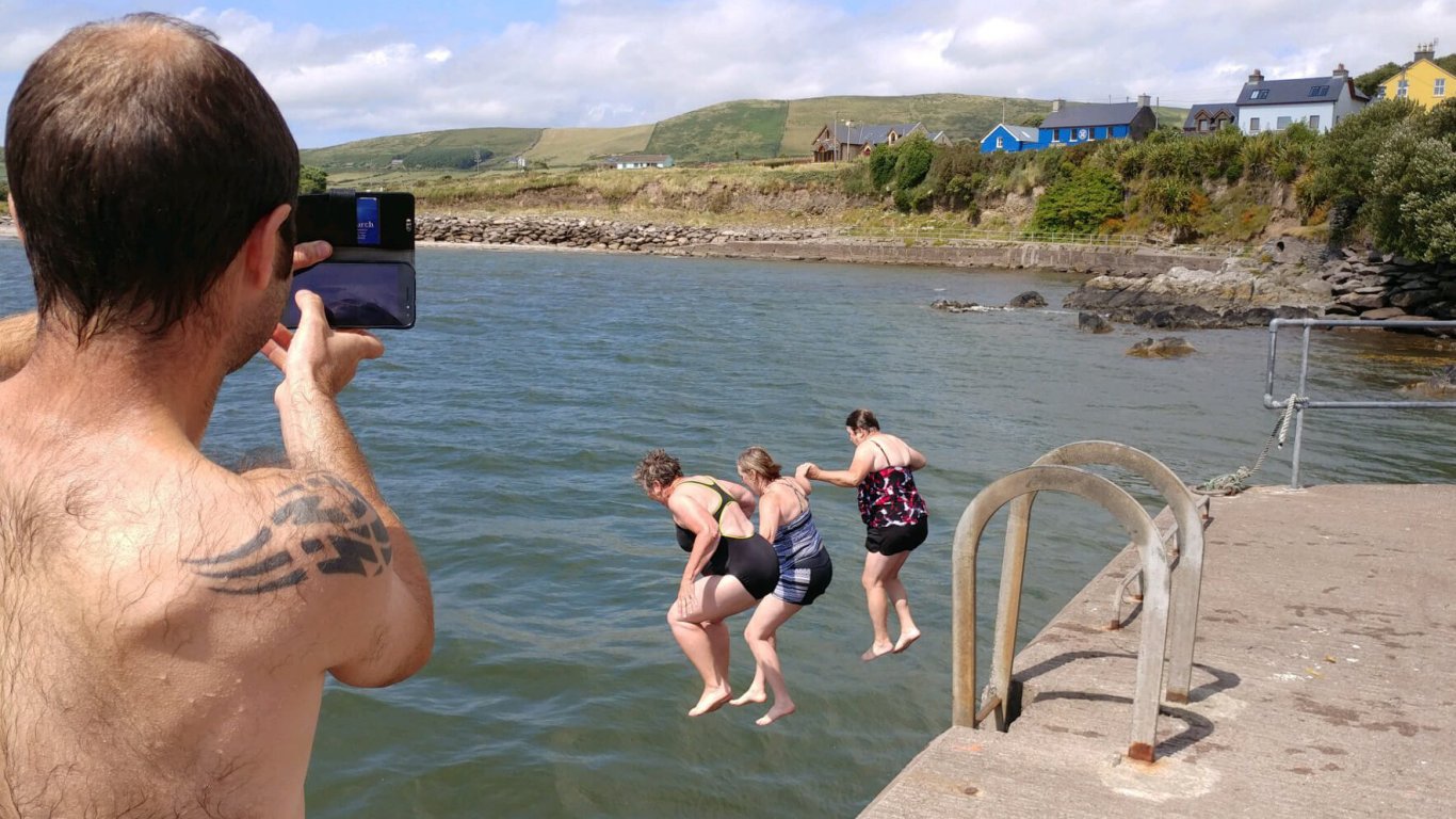 Three ladies jumping off a pier into the sea during summer in Ireland