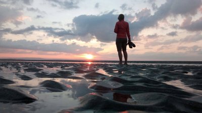 A woman standing on a beach with the back to the camera as the sun is setting 