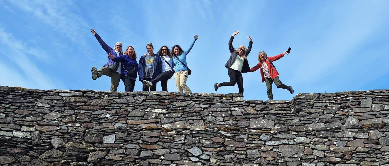 Tour group posing in Ireland in a funny way on a stone wall with a blue sky in the background