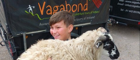 Kid holding large sheep on Vagabond family tour of Ireland