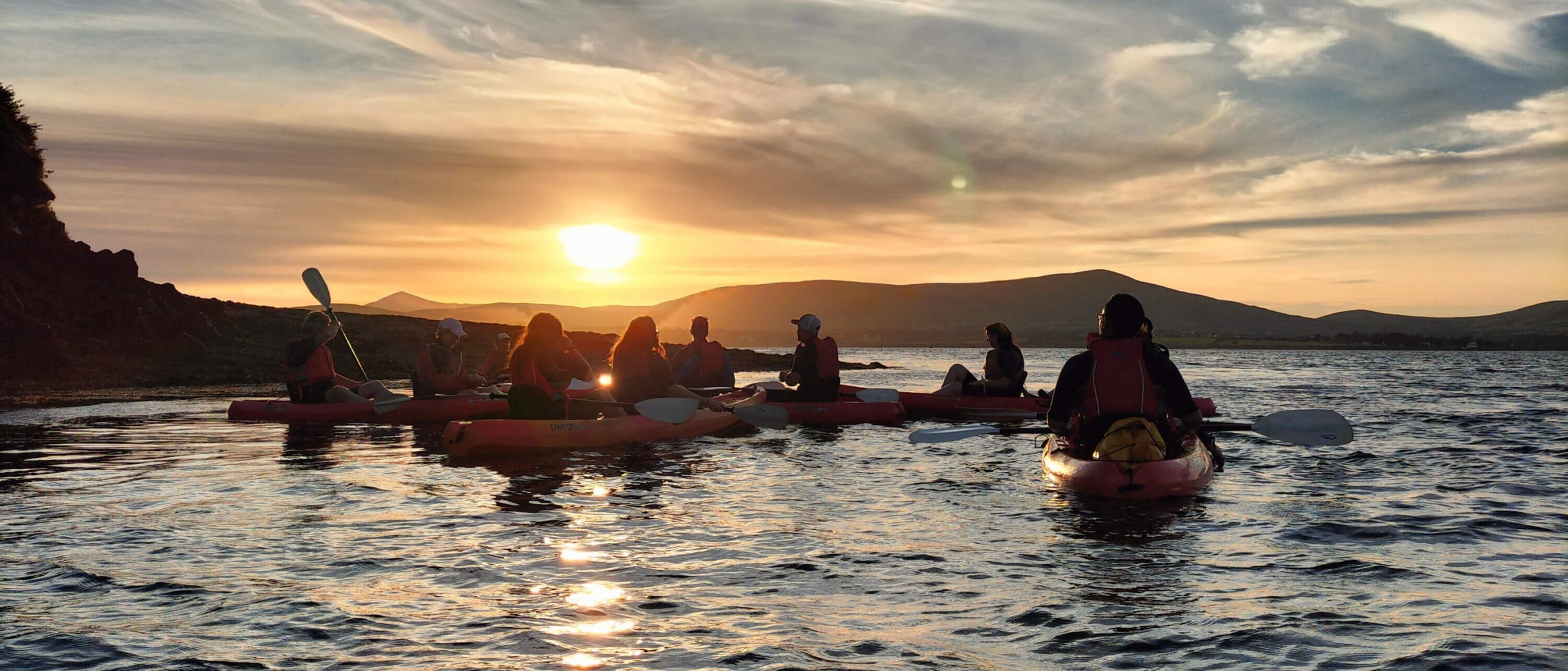 Adventure tour group kayaking in Ireland with sunset