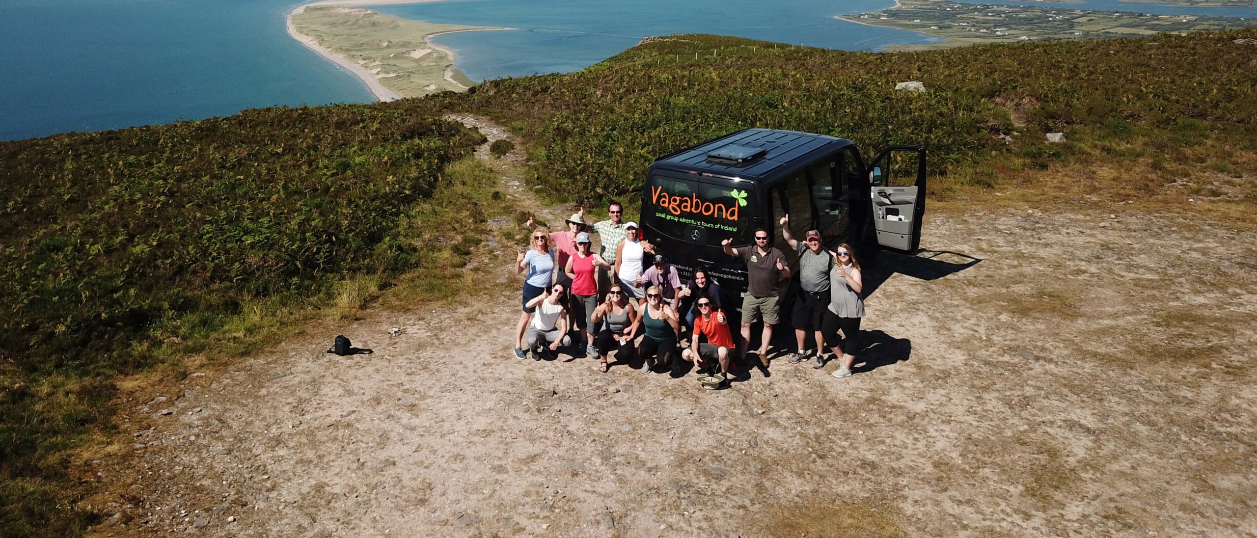 Vagabond Tour vehicle with group in scenic location in Ireland waving at camera from drone