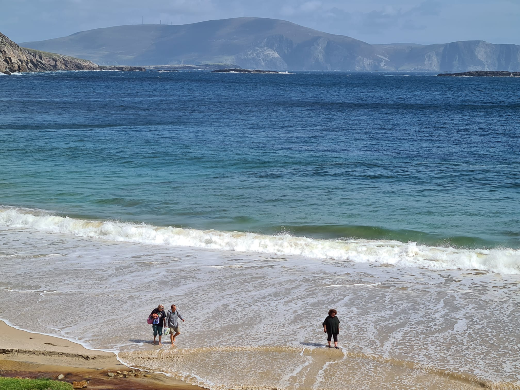 three guests walking on the beach in the sun with a mountain in the background