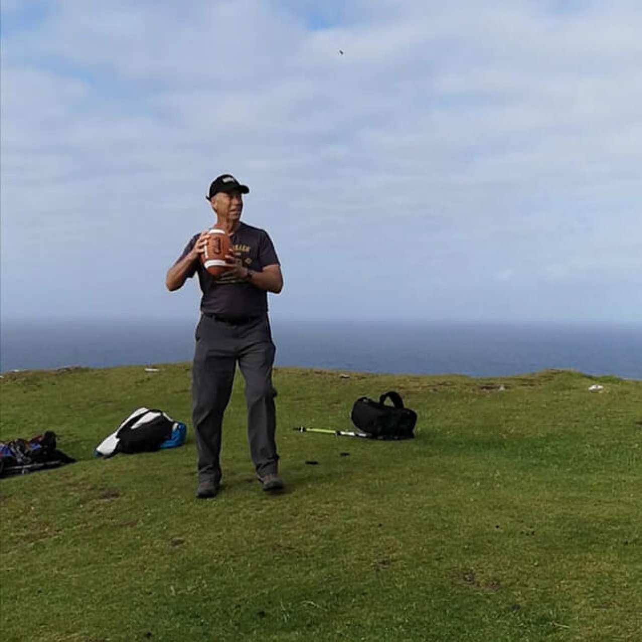 A man holding an american football getting ready to throw it while standing on Bray Head.