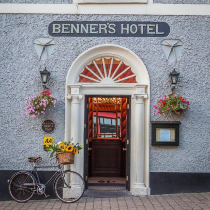 The front door of the dingle benners hotel with a bike outside and flower hanging baskets