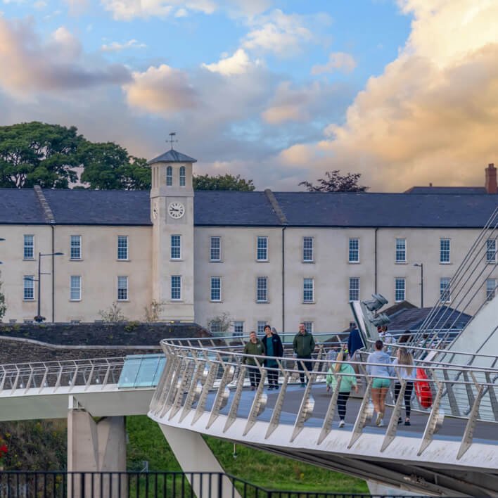 Exterior of Ebrington Hotel in Derry, Northern Ireland, showing walkers on the nearby Peace Bridge