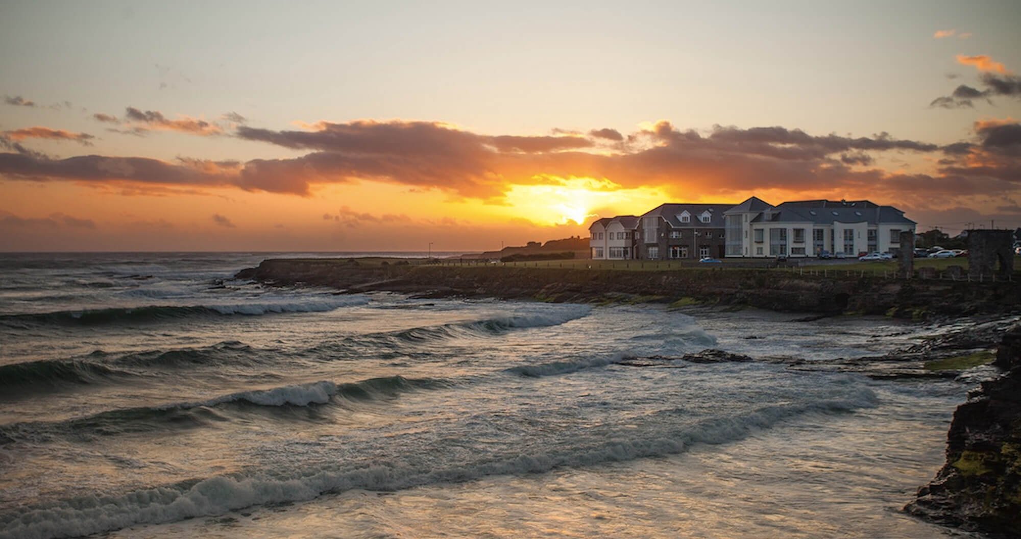 Sunset over the Armada Hotel beside waves at Spanish Point beach in Ireland