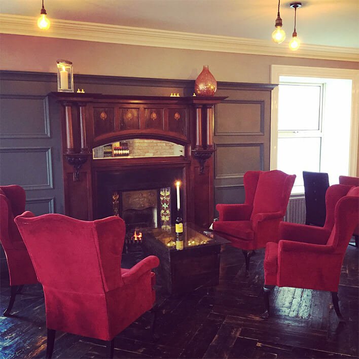 Cosy chairs in front of a fireplace in the living room of Arnolds hotel 