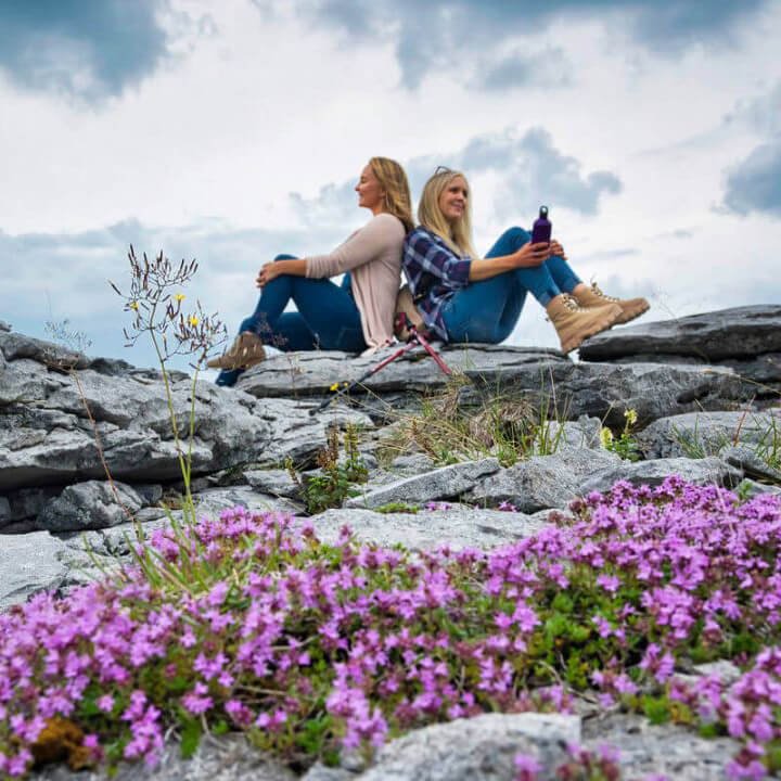 Two women sitting on a rock beside some flowers in The Burren in Clare, Ireland