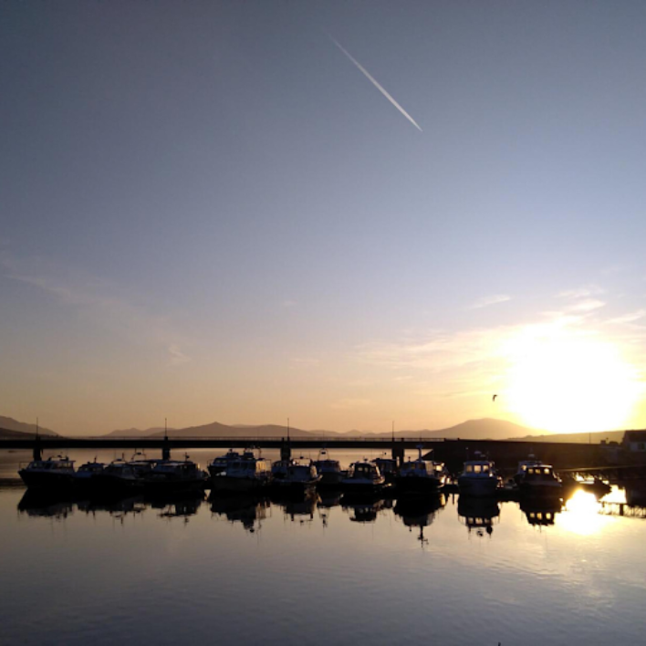 A sunset in Portmagee harbour behind a row of boats