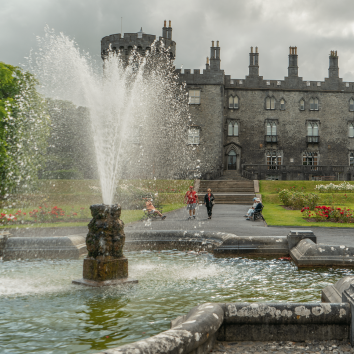 A fountain spraying water with kilkenny castle in the background
