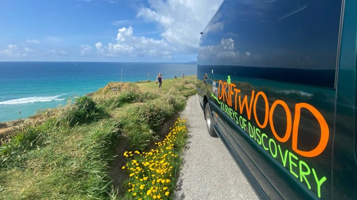 Side view of tour vehicle parked beside a sunny coastline and flowers