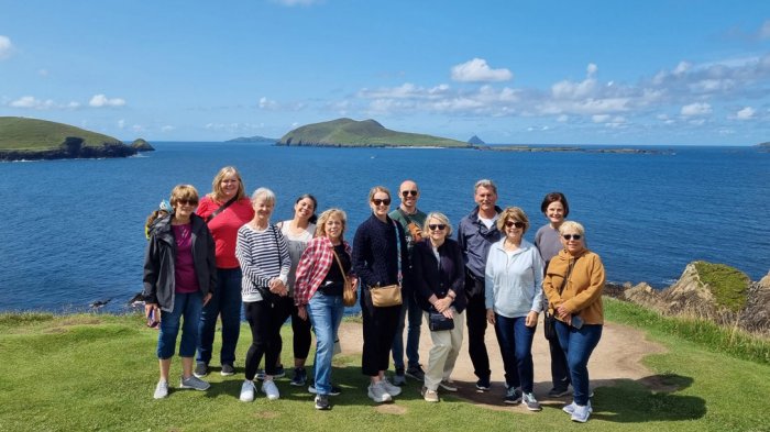 Happy tour group standing on a headland in Ireland with blue skies and ocean
