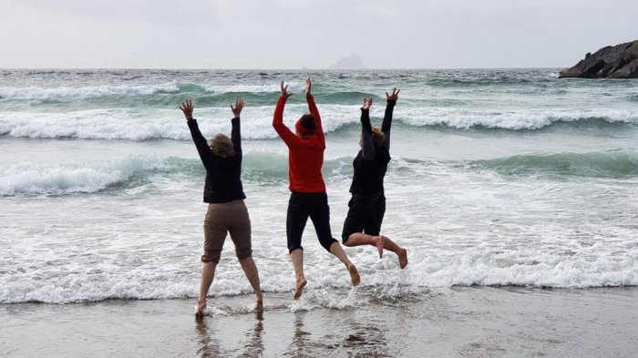 Three tour guests jumping in the waves on a beach in Ireland