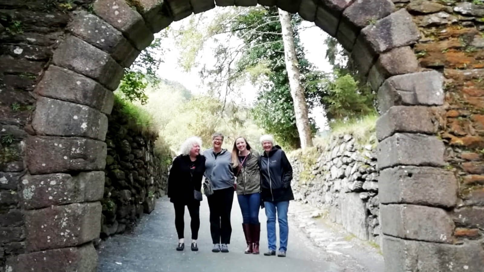 Smiling Driftwood tour group standing in an old arch in Glendalough, Ireland