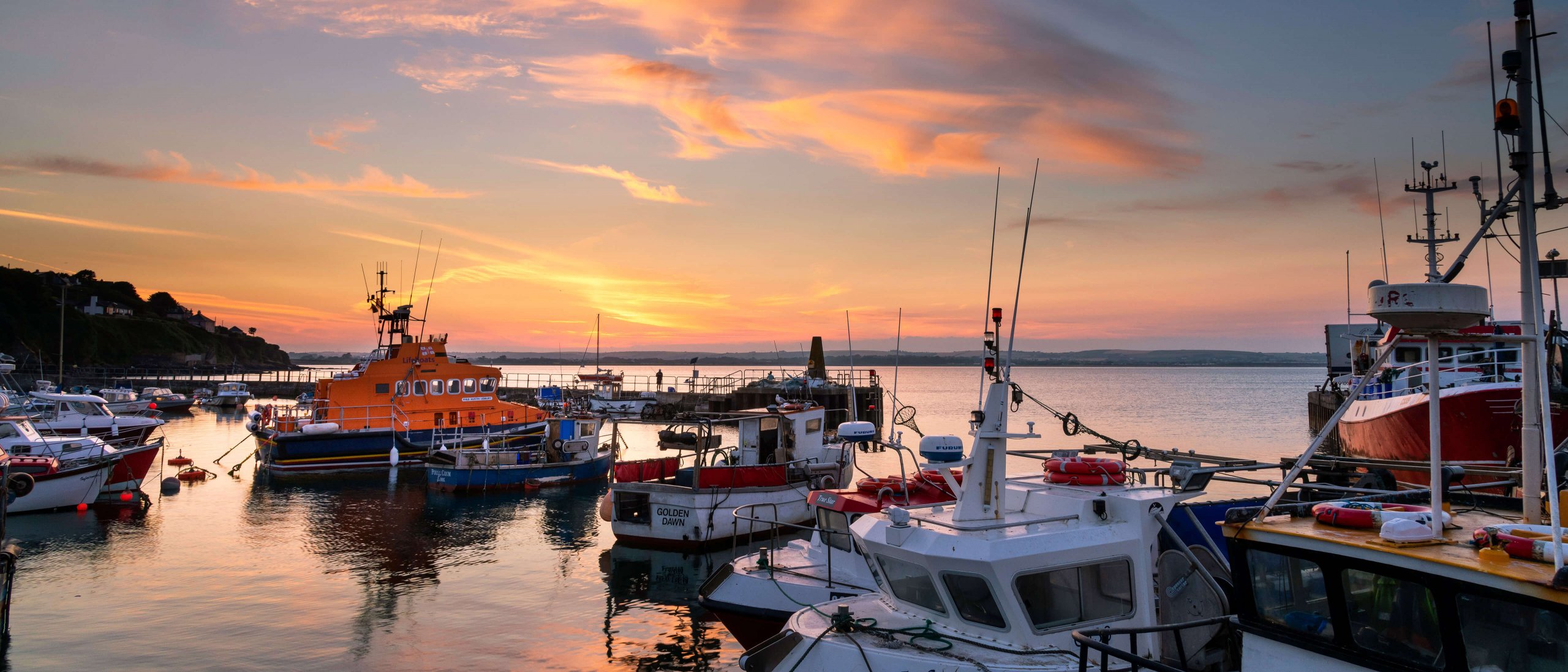 A view of Ballycotton harbour during the sunset with fishing trawlers and other boats in view.