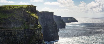Dramatic shot of very small people standing on top of the Cliffs of Moher in Ireland