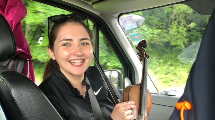 Ireland tour guide smiling and holding a violin in the front seat of a tour vehicle in Ireland