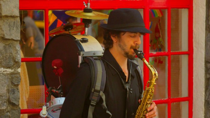 One man band playing saxophone in front of red window in Ireland