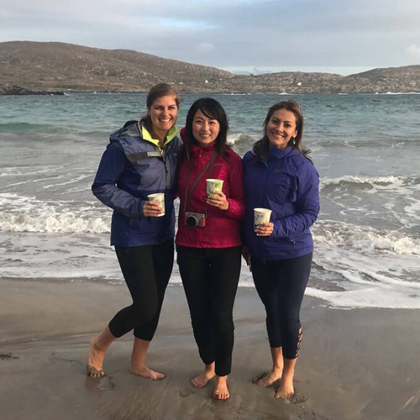 Three Vagabond tour guests enjoy an Irish coffee barefoot on a beach