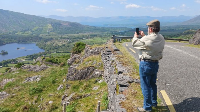 A man standing on the healy pass taking a photo of glanmore lake