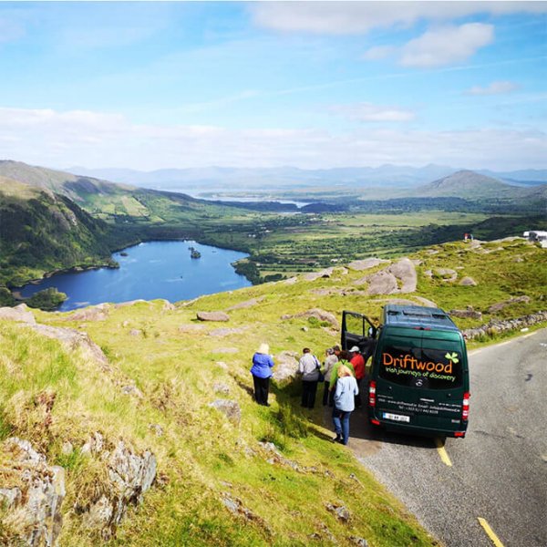 A Drifter tour vehicle parked in a scenic location on the Healy Pass in Ireland while a group of Driftwood tour guests enjoys the mountain and lake view