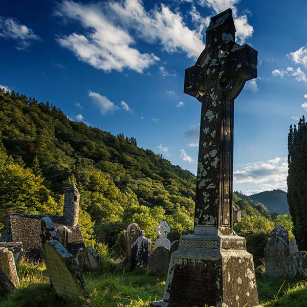 Celtic cross in Glendalough graveyard with church tower in background