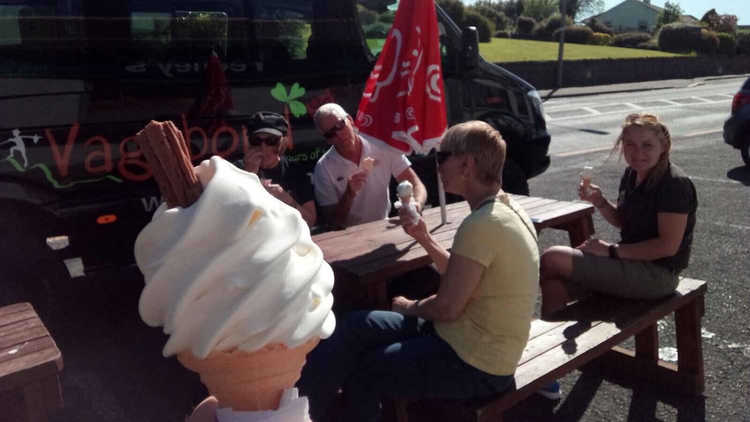 Ice cream cone with chocolate flake in the foreground, with Vagabond tour guests and tour vehicle in the background, slightly out of focus